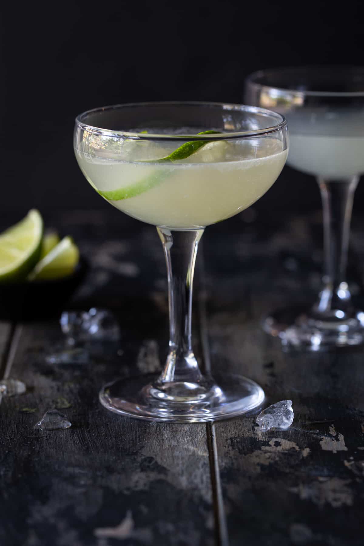 Classic Daiquiri cocktail in a Champagne Coup glass garnished with lime twist sitting on a dark table