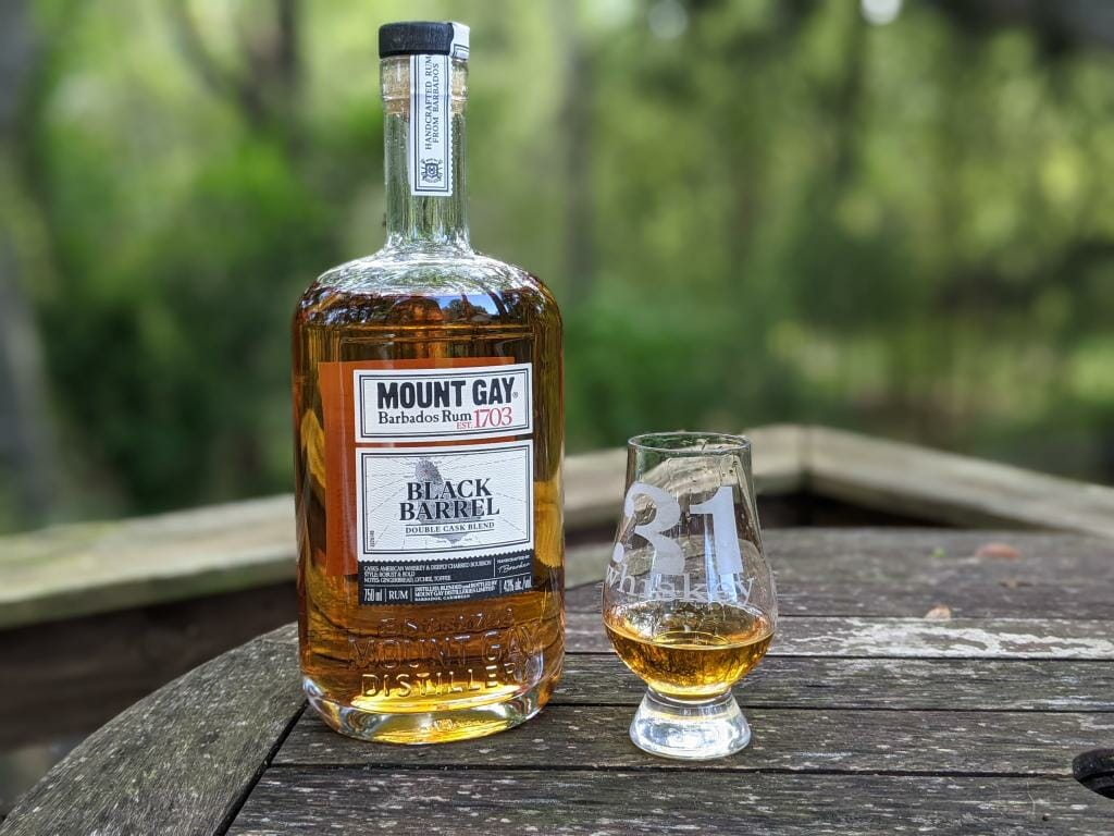 Bottle of Mount Gay Black Barrel rum with small tasting glass sitting on top of wooden barrel